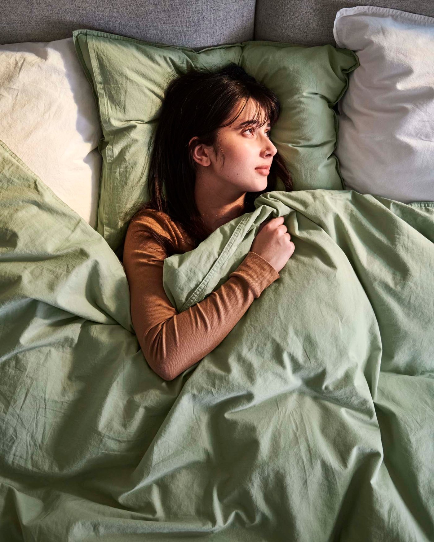 A close-up of a person lying in a bed with light green bedlinen.