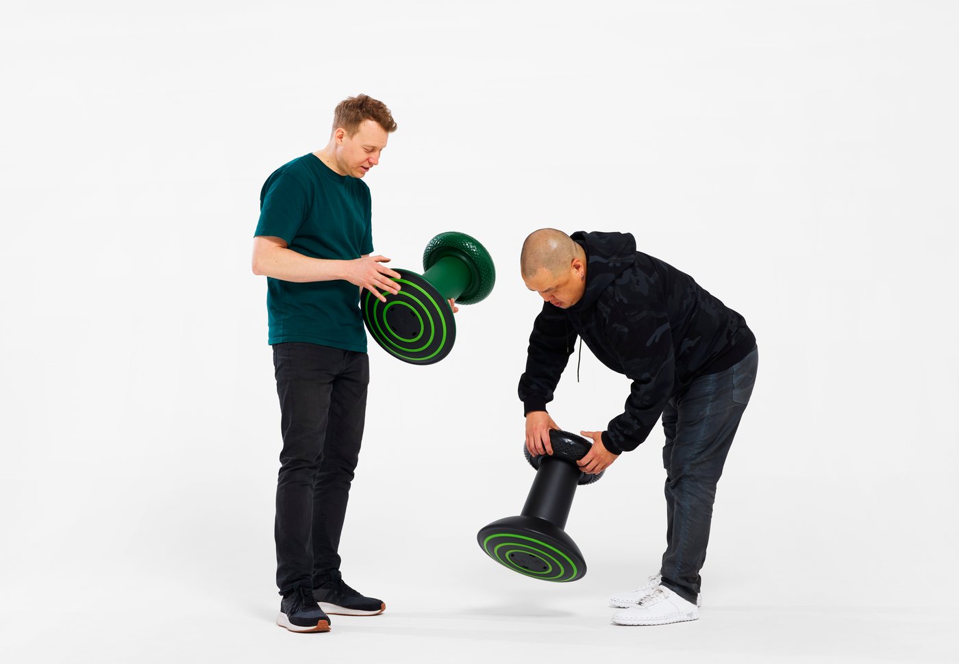 Two designers examining thumbstick-inspired stools against a white studio background.