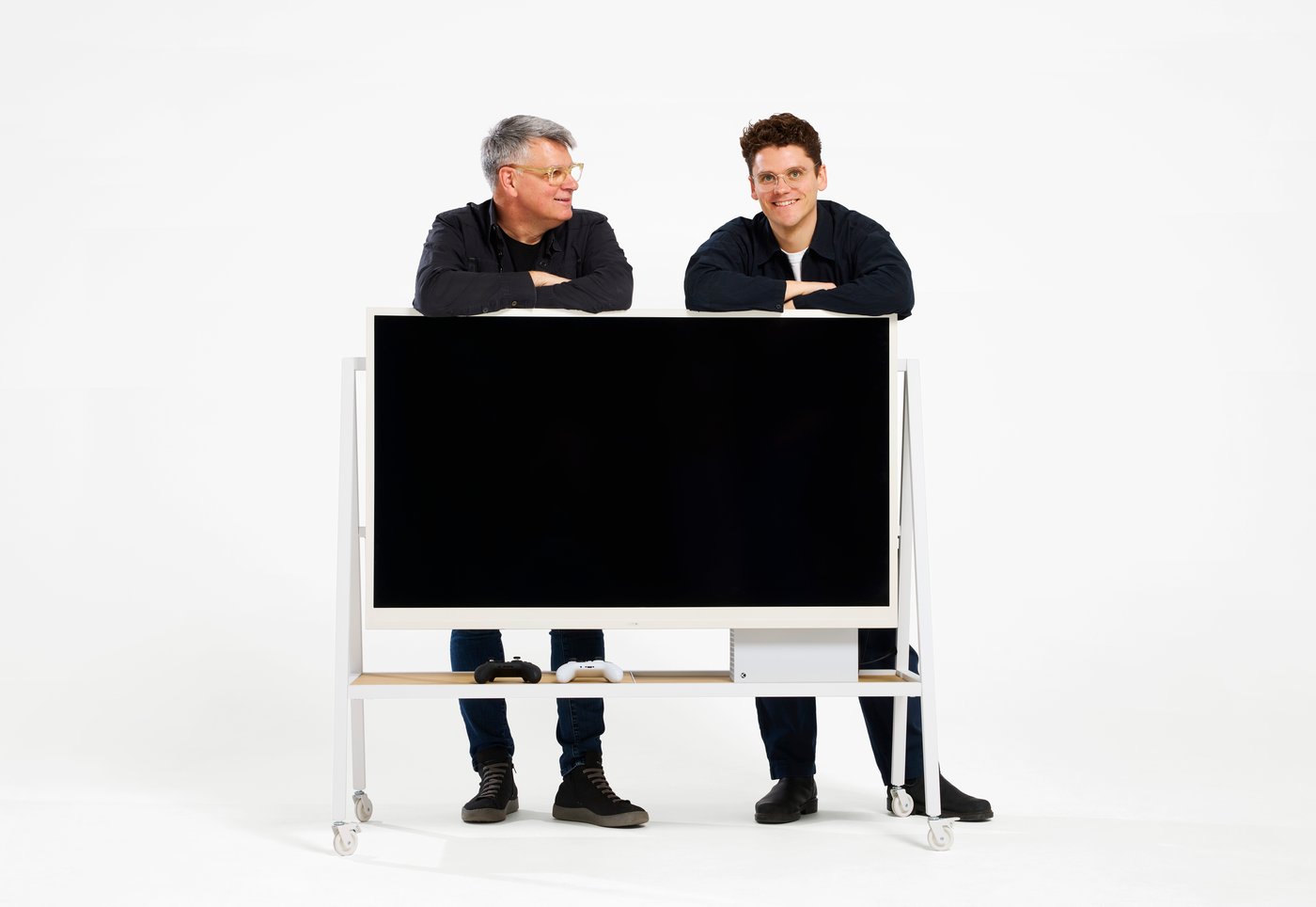 Two designers standing behind a YXSTABY mobile TV stand with shelf and castors.