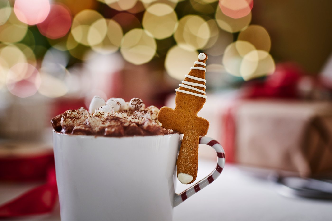 A hot drink topped with whipped cream and chocolate shavings beside holiday ginger bread.