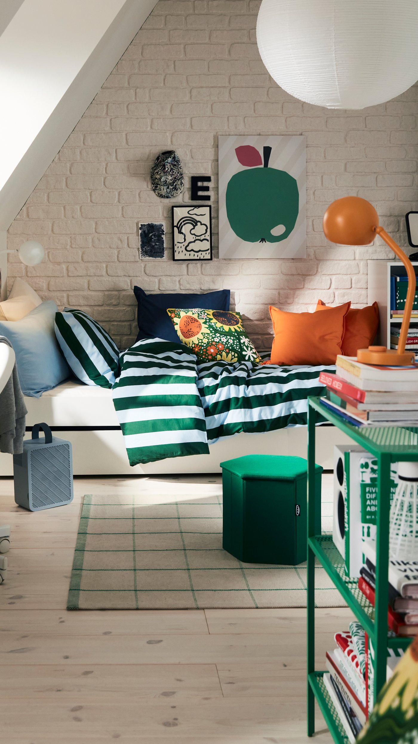 A single bed with bright cushions and a light blue and dark green striped bed linen in a green, white and orange attic space.