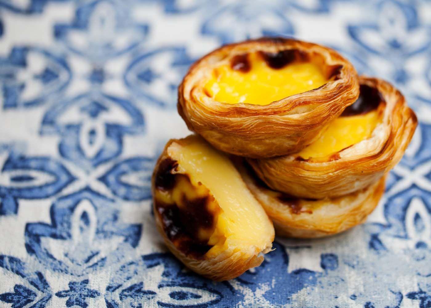Portuguese custard tarts are stacked on a tile surface.