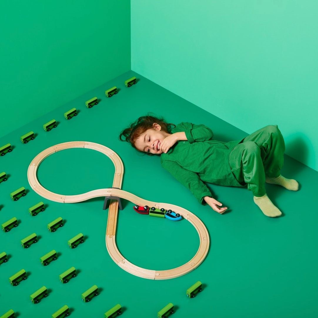 A child lying on a green floor next to toy train track.