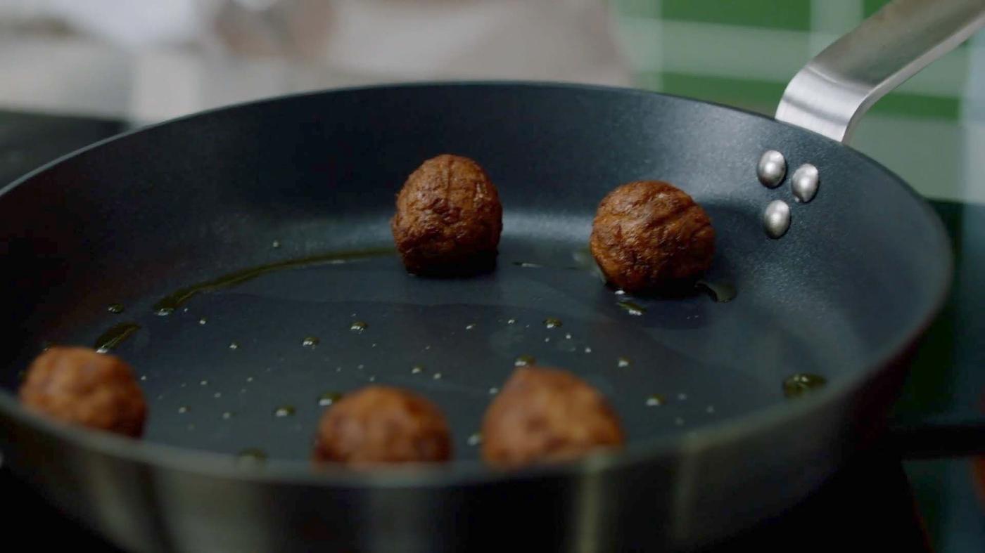 A man and a woman talk about plant balls. They are cooking in a kitchen.