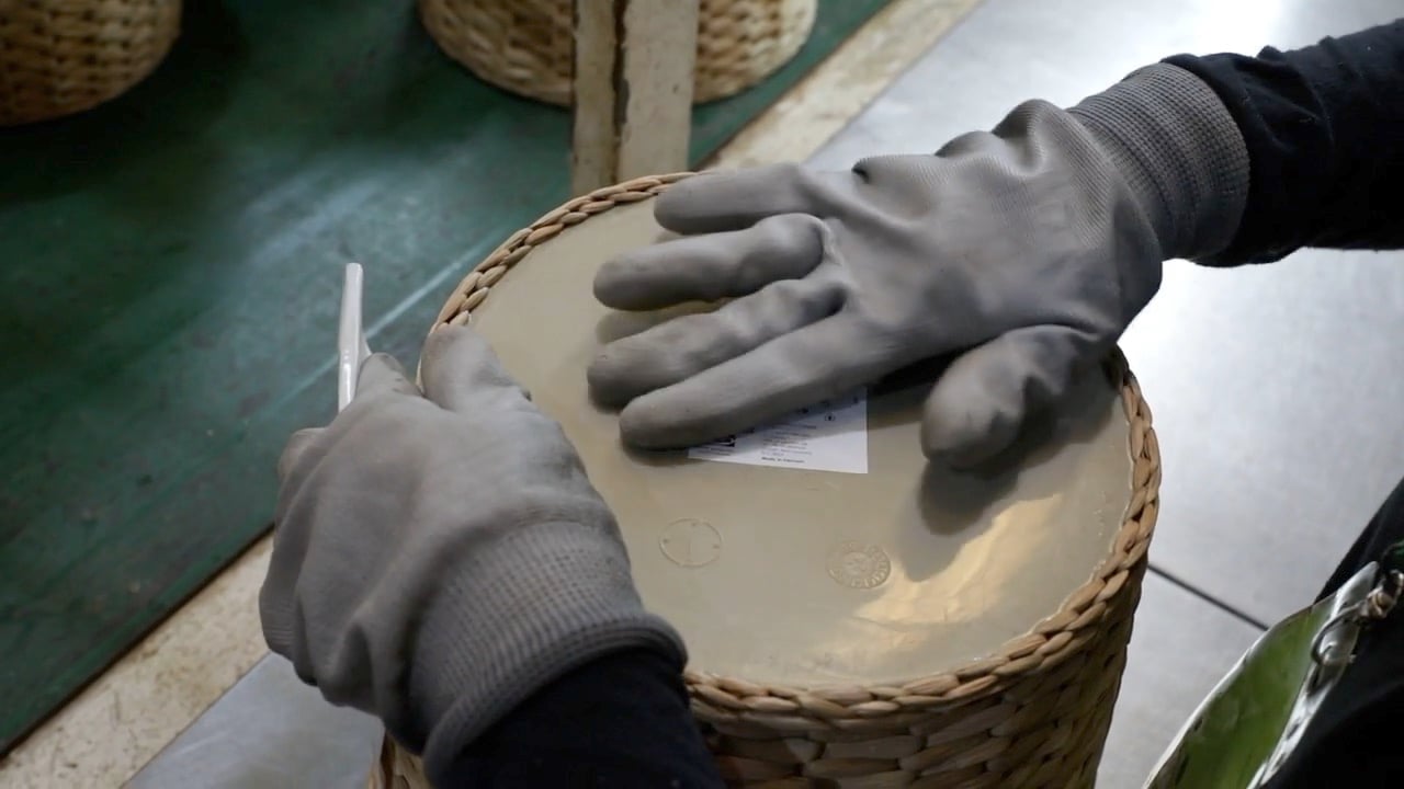 A pair of hands wearing gloves pastes a label onto the bottom of a plant pot.