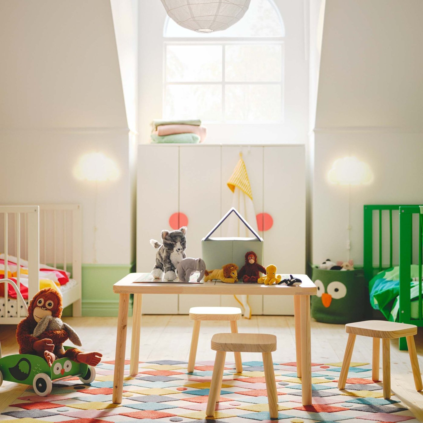 A white children's room with colourful furniture, a natural coloured wood table and chairs in the centre and a window in the background.