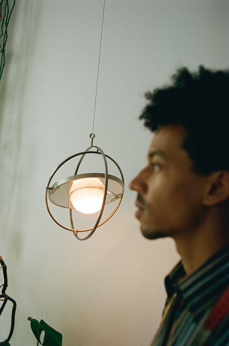 A person's out-of-focus side profile with a SAMMANLÄNKAD LED solar-powered table lamp hanging from the ceiling in the background.