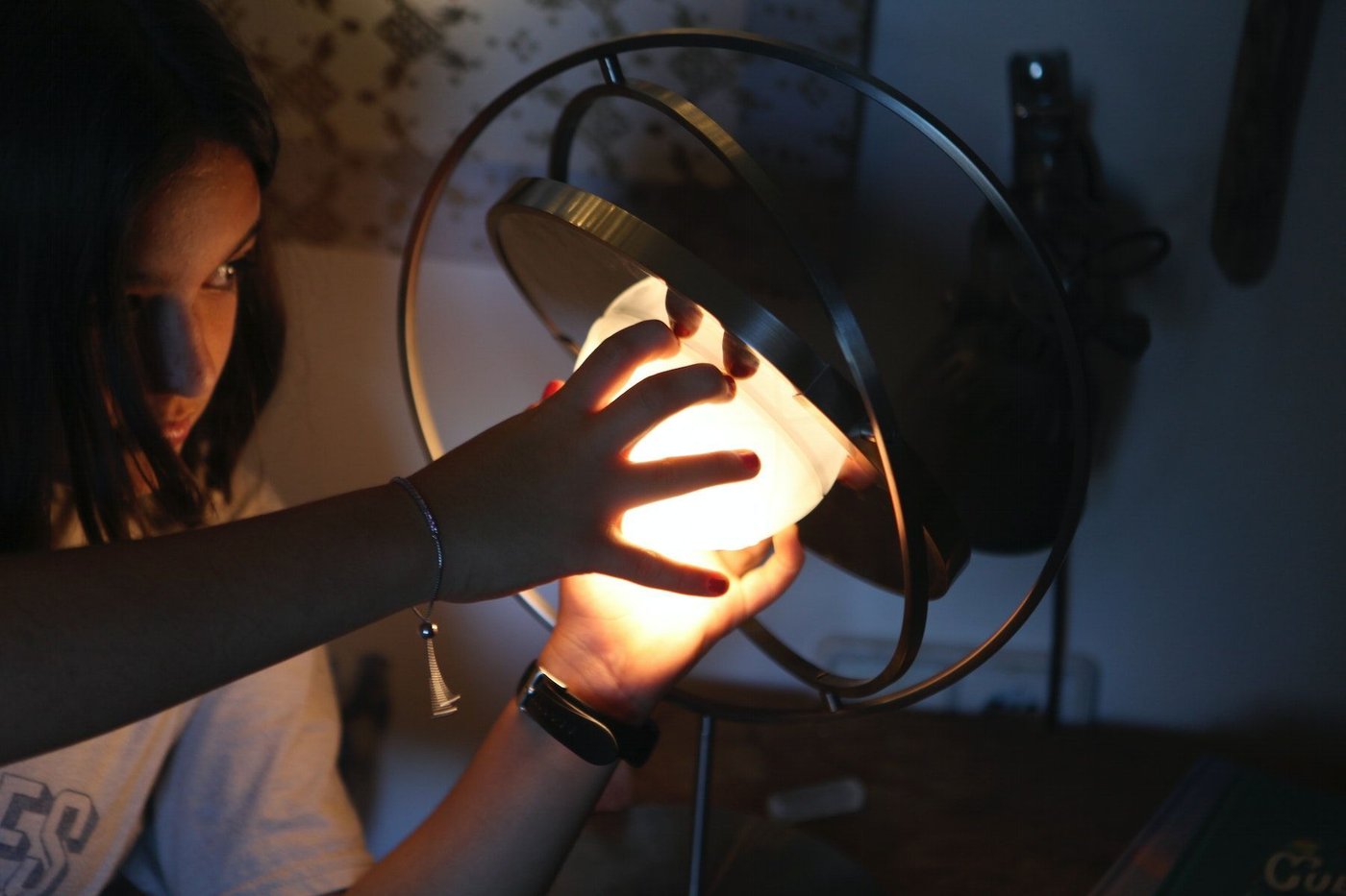 A child reaches out with both hands to detach the illuminated light source from the SAMMANLÄNKAD LED solar-powered table lamp. 