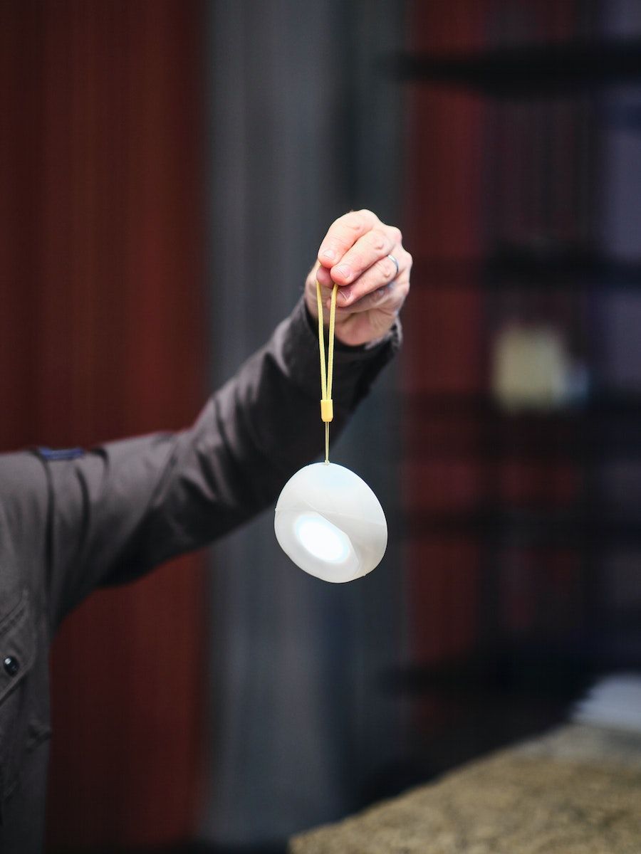 An extended arm holding the SAMMANLÄNKAD solar-powered lighting by its yellow strap. 