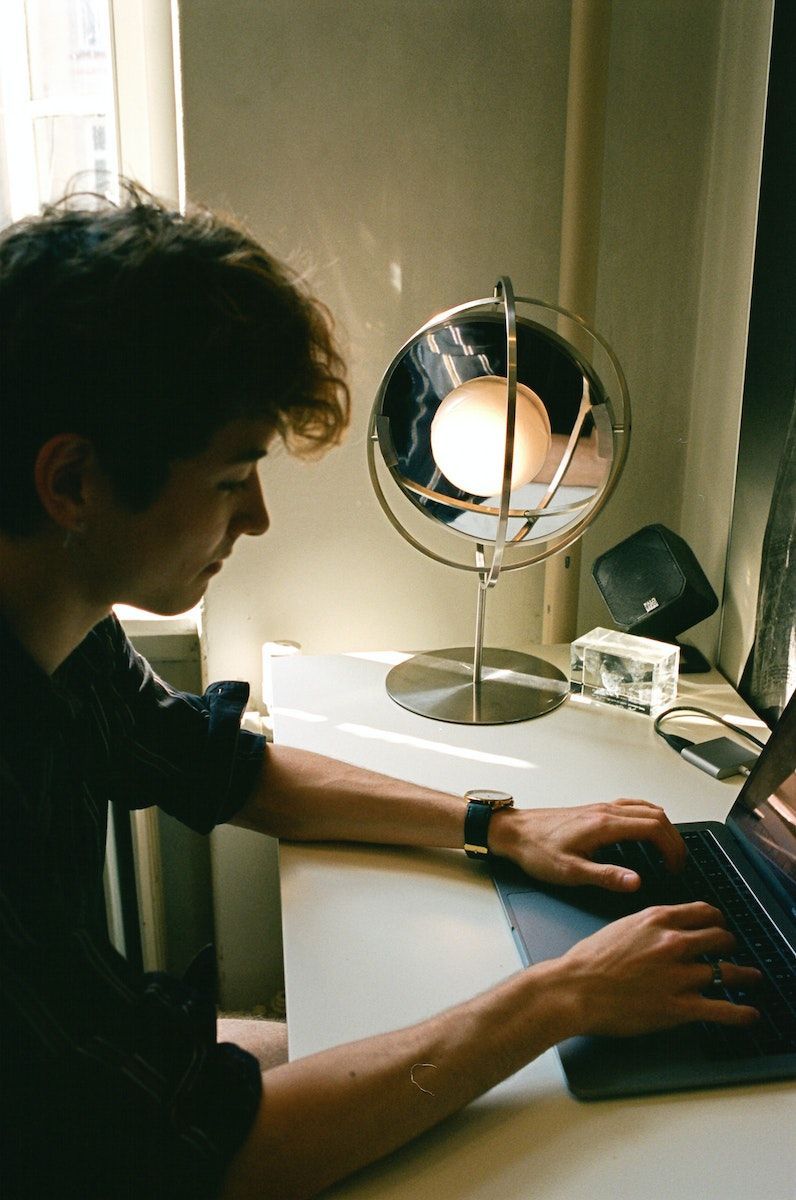 A person working on their laptop, with an illuminated SAMMANLÄNKAD table lamp on the desk nearby.