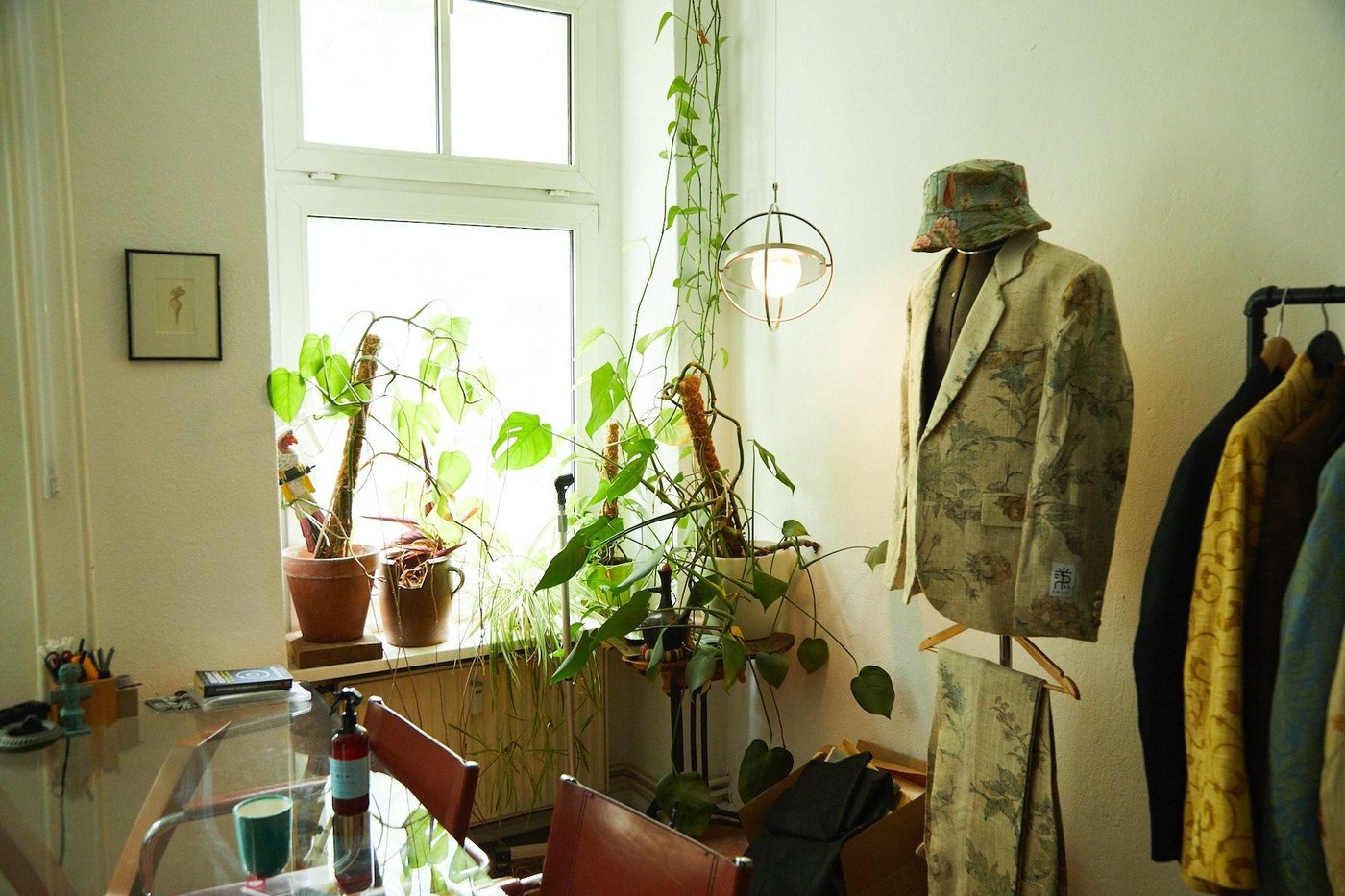 A SAMMANLÄNKAD lamp hangs as a pendant lamp from the ceiling of a sunny room with a mannequin and clothes rail.