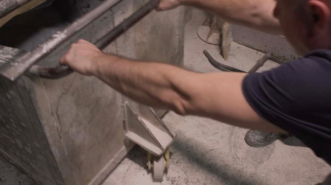 A factory co-worker pulling out a metal vat on wheels.