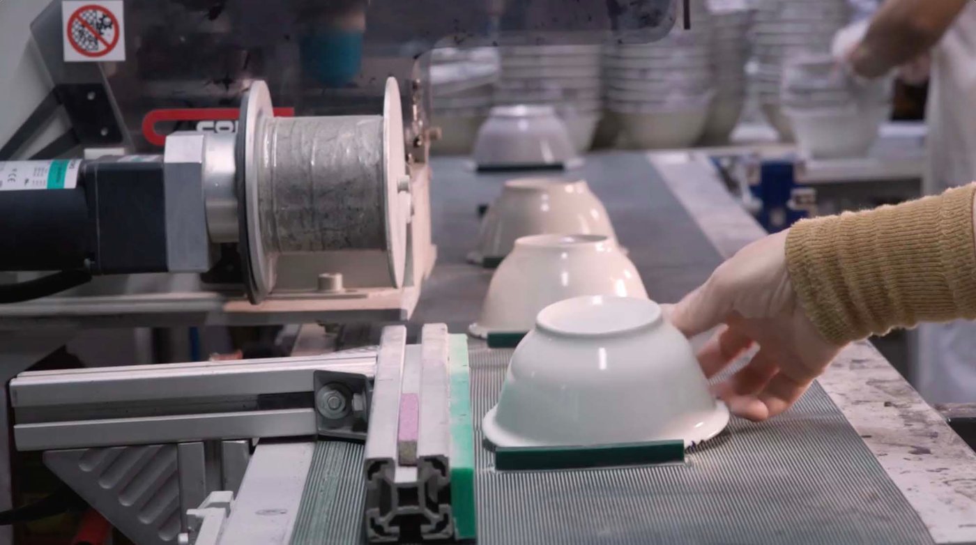 A hand reaches for a SILVERSIDA bowl on a factory conveyor belt.