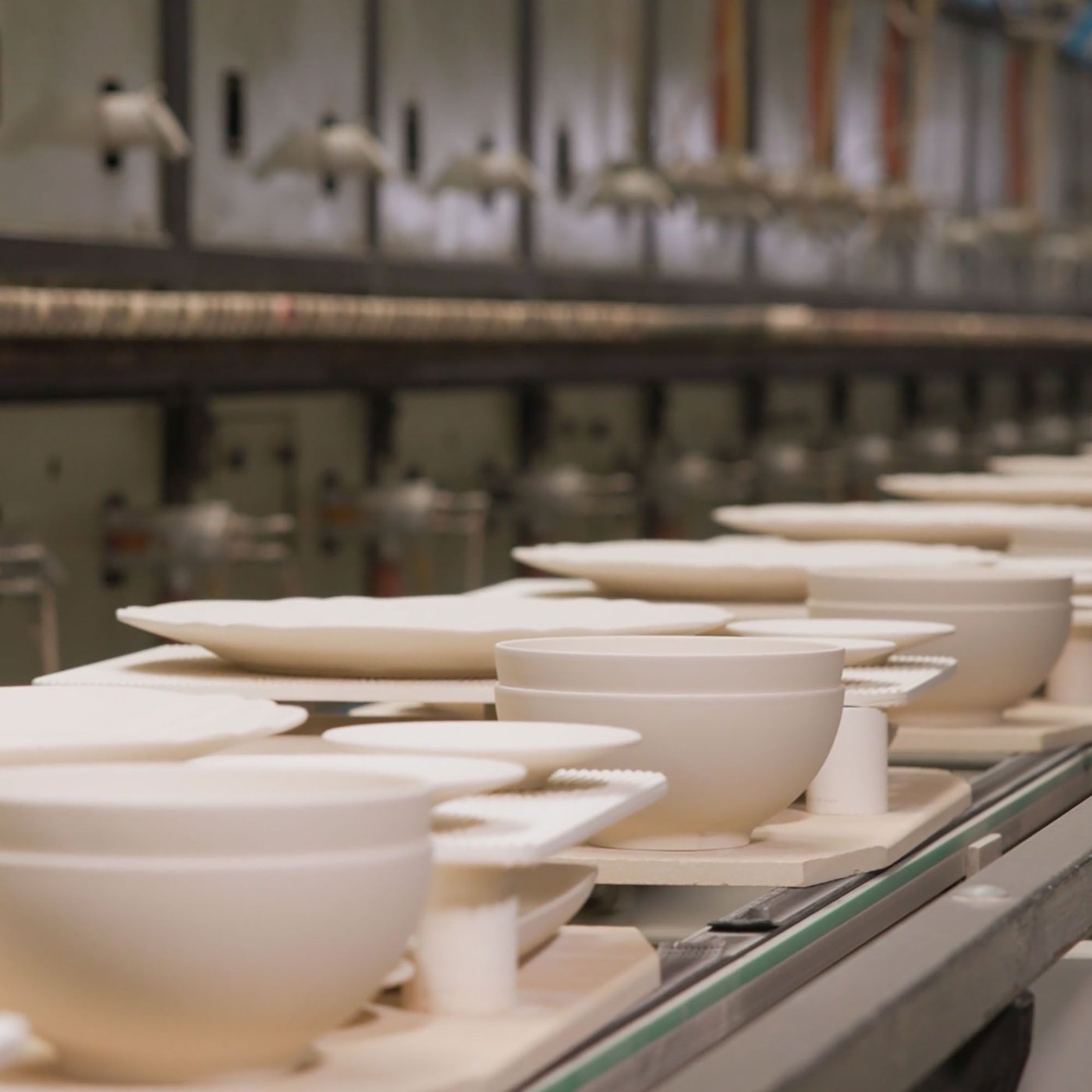 Unglazed ceramic dinnerware on a conveyor belt.