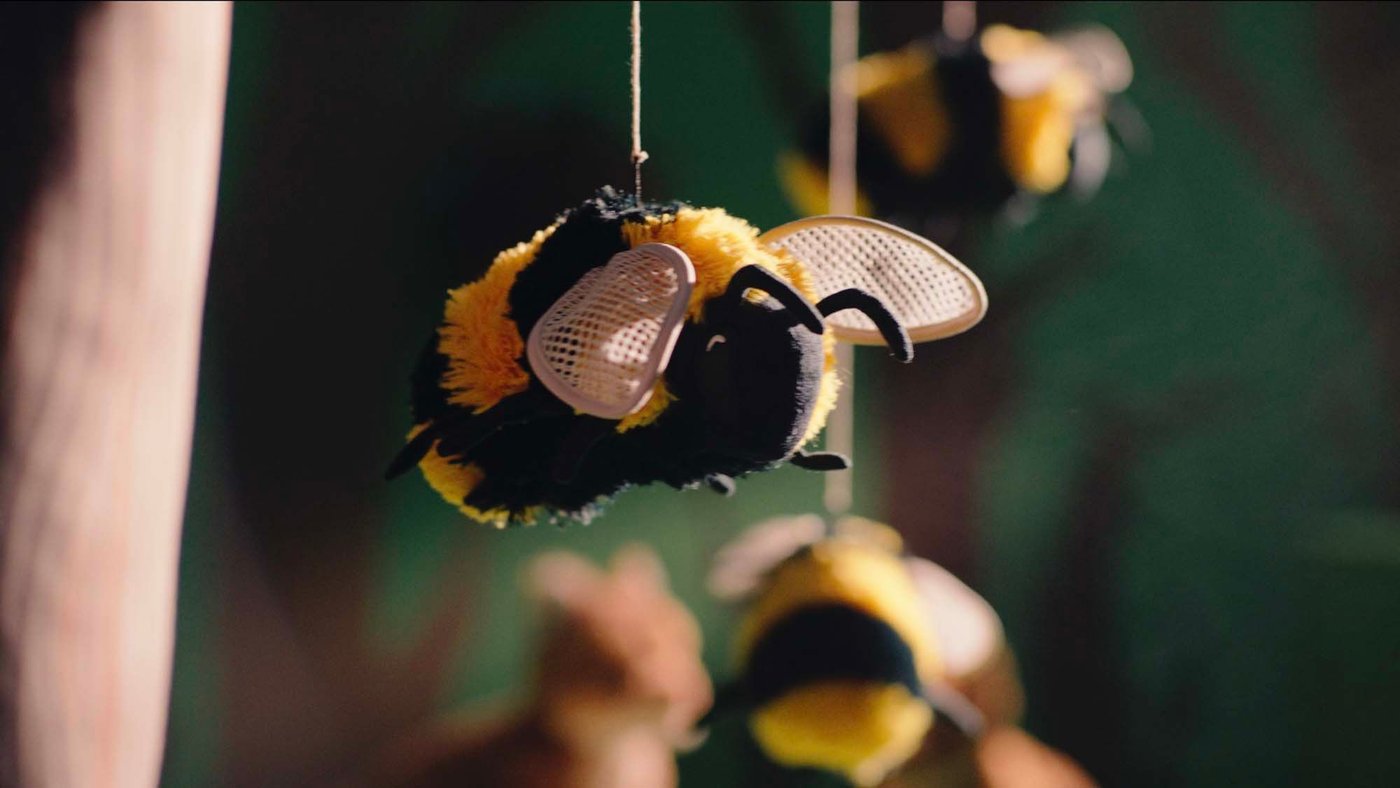 Three SKOGSDUVA bumblebee/black yellow soft toys hovering in the air against a green background.