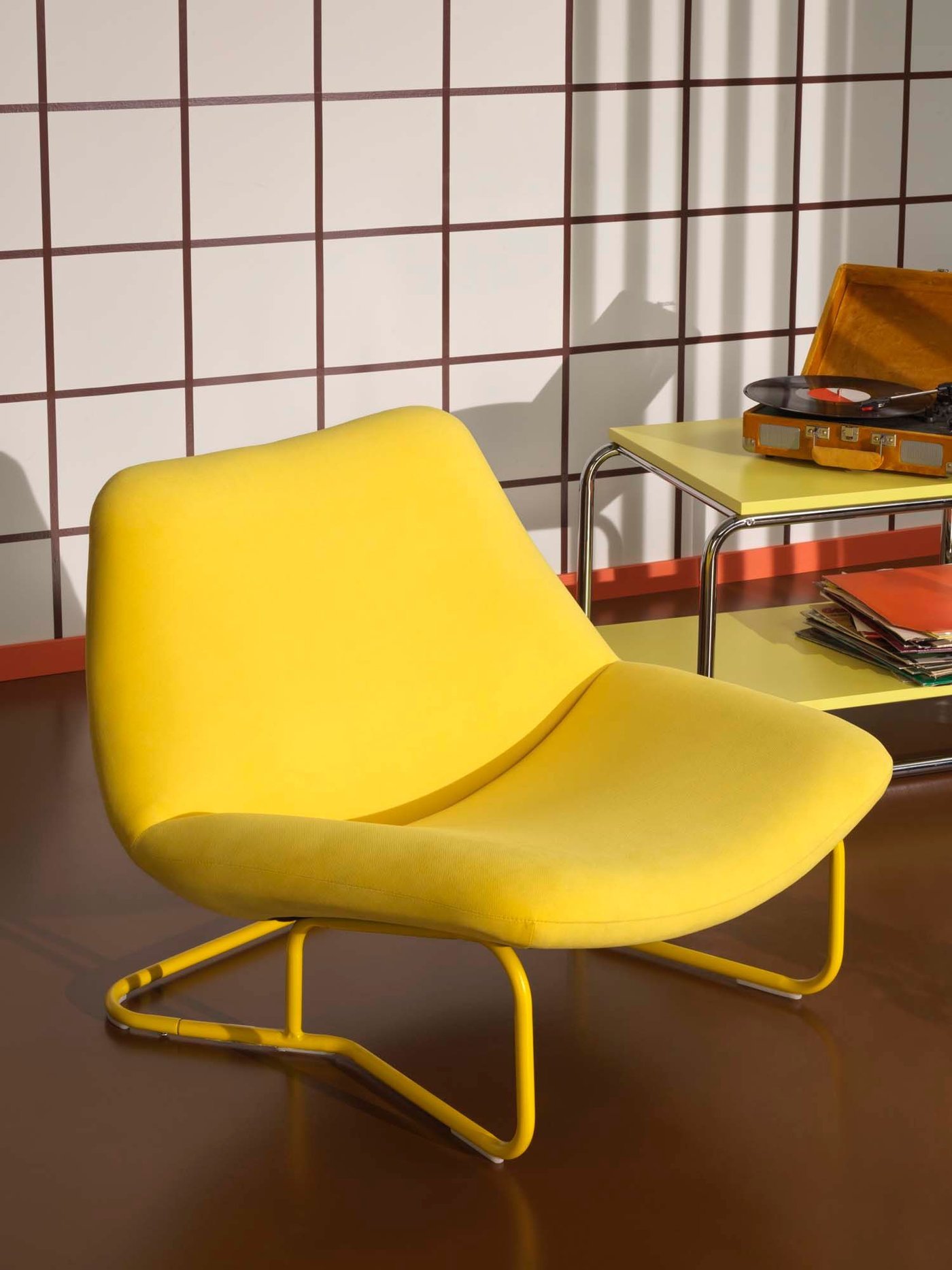 A yellow chair stands in front of a yellow side table, against a chequerboard background.