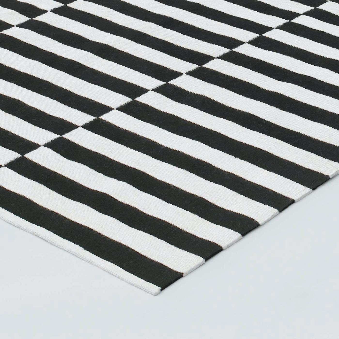 Closeup of a corner of a black and white striped STOCKHOLM wool carpet.