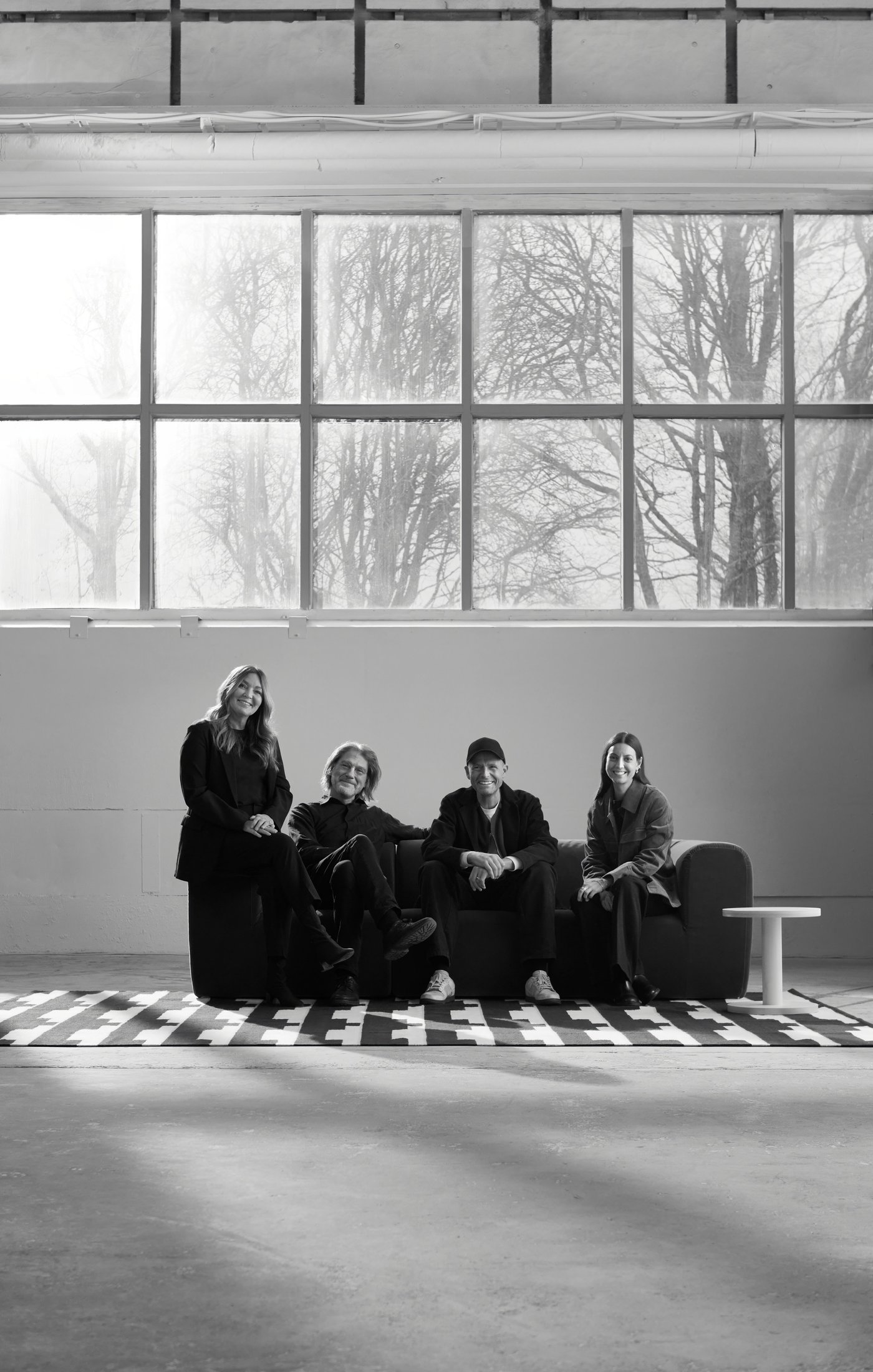 Black and white portrait of three designers and one creative leader sitting in a big industrial room, in a sofa.