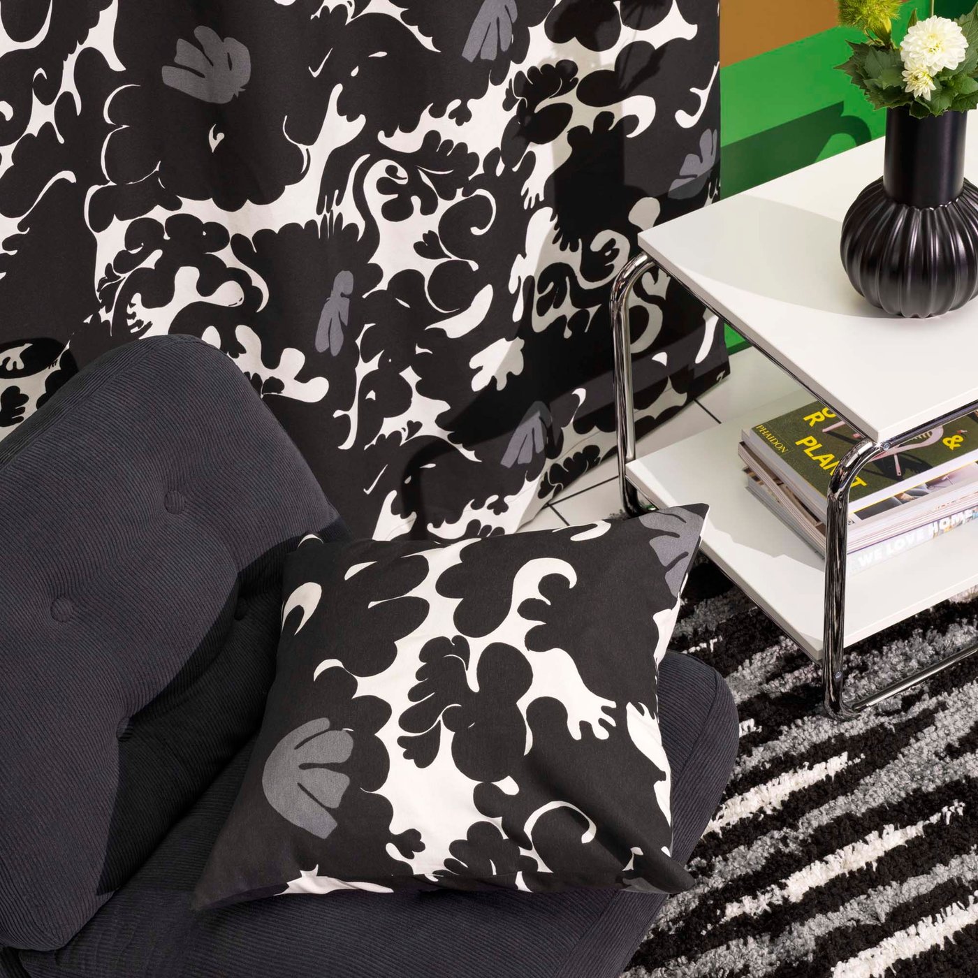 Matching black, white and grey patterned curtains hang behind a chair and side table. A cushion in the same print sits on the chair.