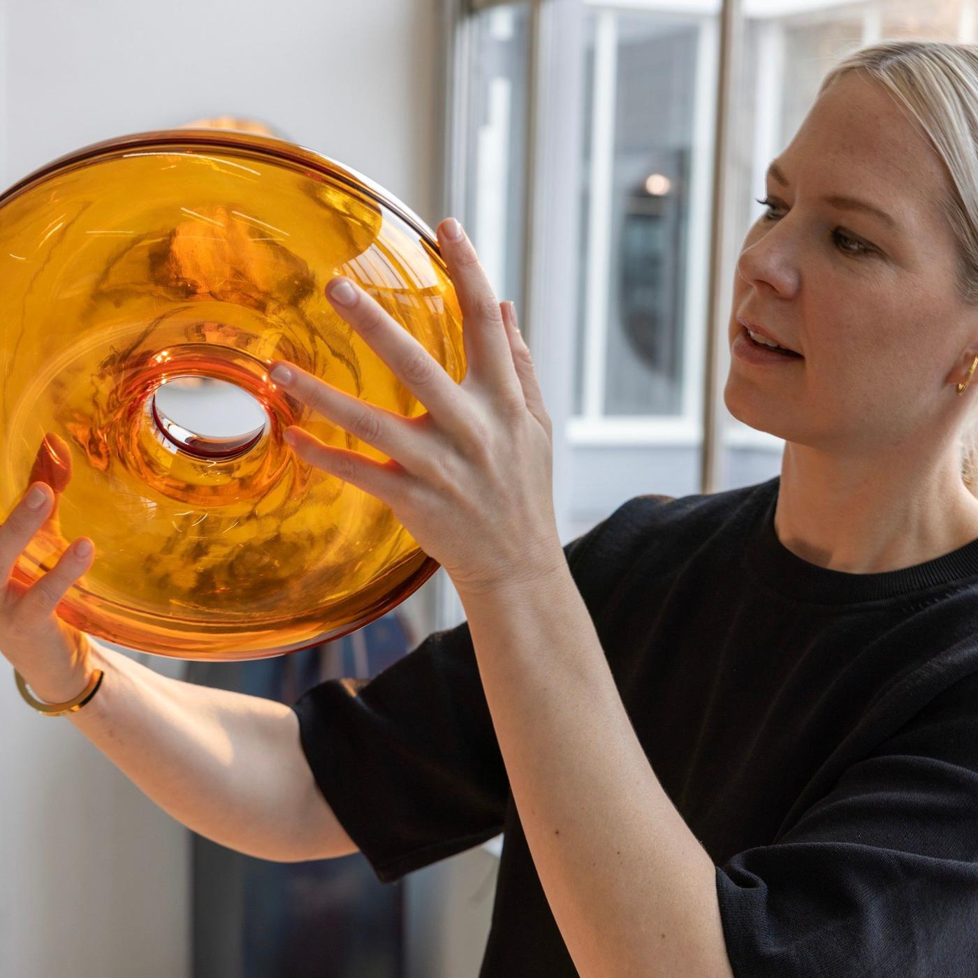 A woman in a black shirt holding an orange coloured glass lamp in her hands.