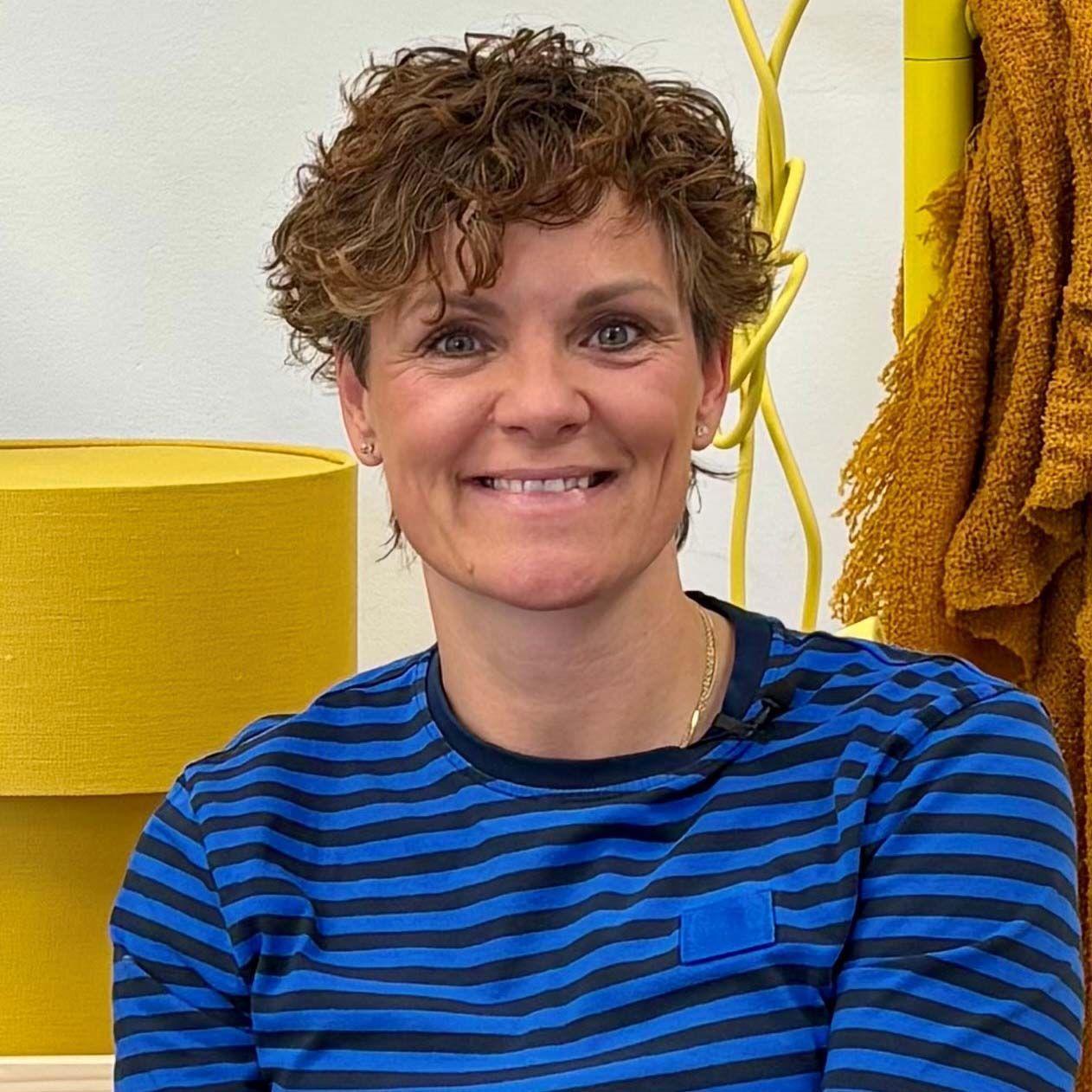 Sandra smiles at the camera, with a yellow table lamp in the background.