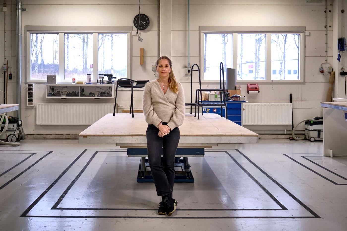IKEA designer Sarah Fager leaning against a work table in a studio setting with two products from the BÄSINGEN collection.