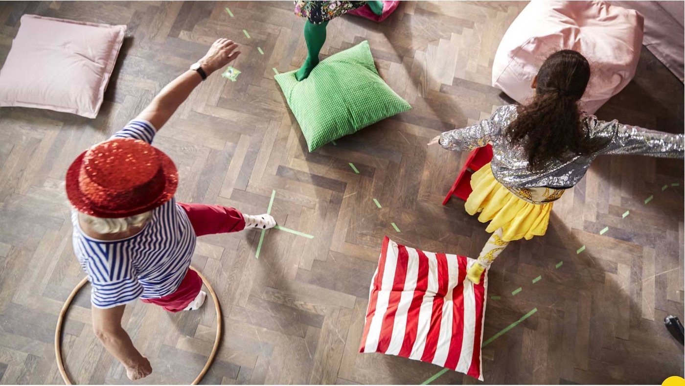 An aeriel image of two children playing. One has one leg in a hula hoop, the other child is jumping from cushion to cushion.
