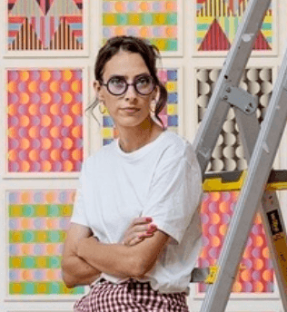 A person with folded arms in front of a wall covered in prints of patterns.