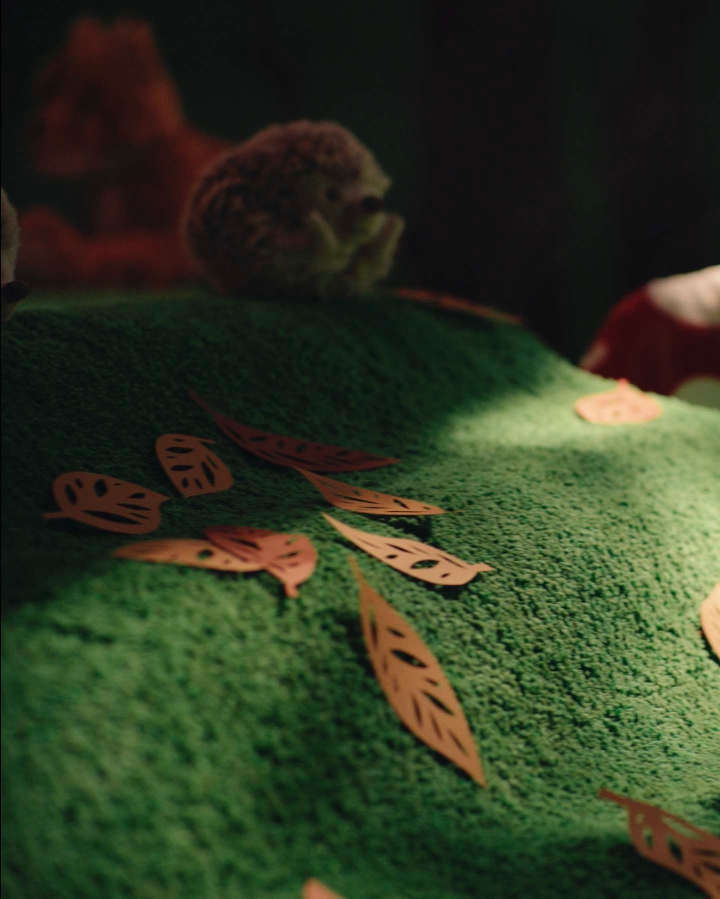 A green slope covered in brown paper leaves with a hedgehog/beige SKOGSDUVA soft toy in the background.