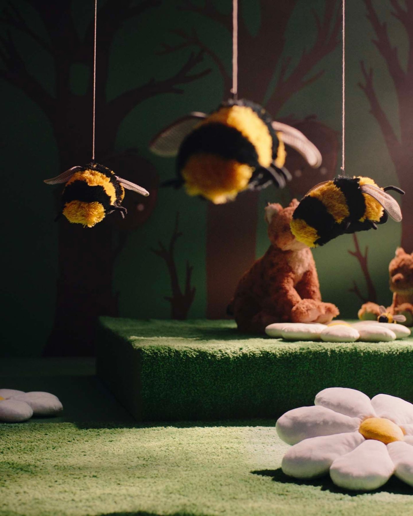Three SKOGSDUVA bumblebee/black yellow soft toys hanging from strings against a green background.