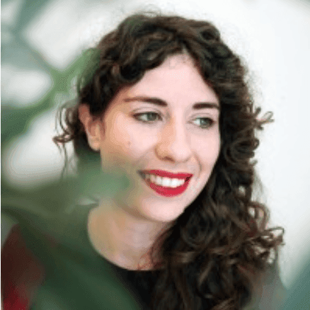 A head and shoulders image of Maria O'Brian, smiling. Her face is slightly obscured by a green branch in the foreground.