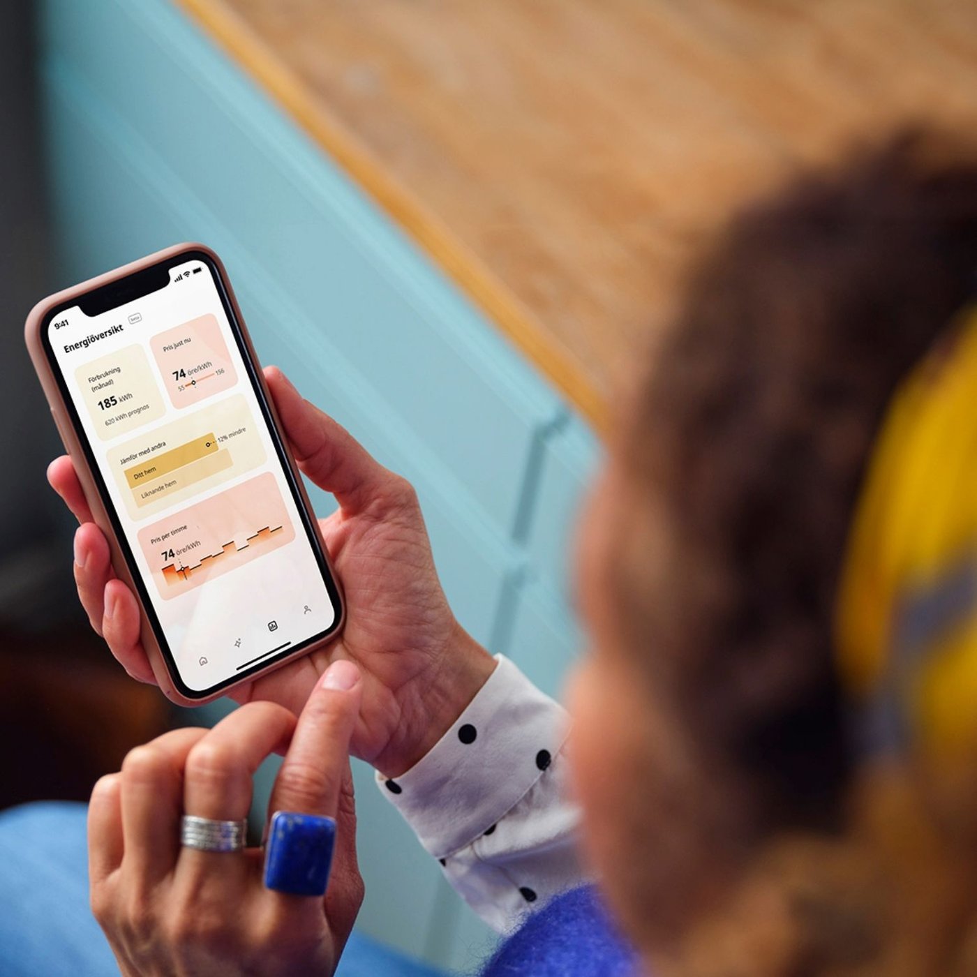A girl with yellow headband is pointing at an iphone touchscreen with her finger, playing with the new Energy Insights feature in the IKEA Home smart app