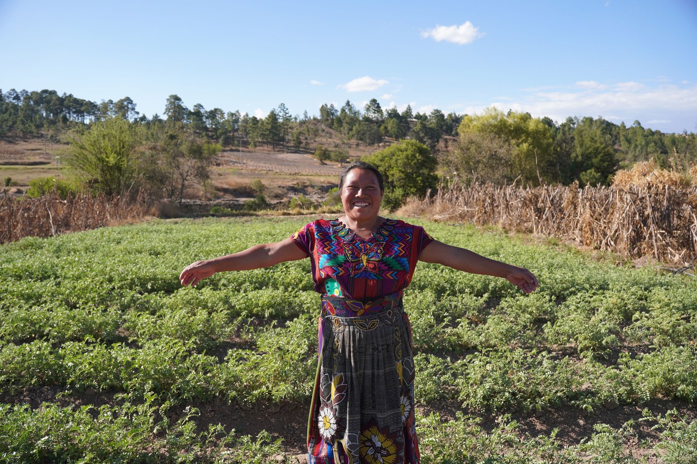 A woman standing in front of a meadow, with her arms open. 