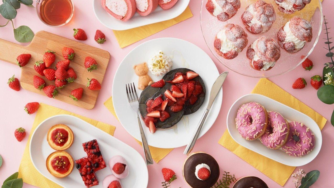 Overhead view of a pink surface decked with an assortment of strawberry desserts.