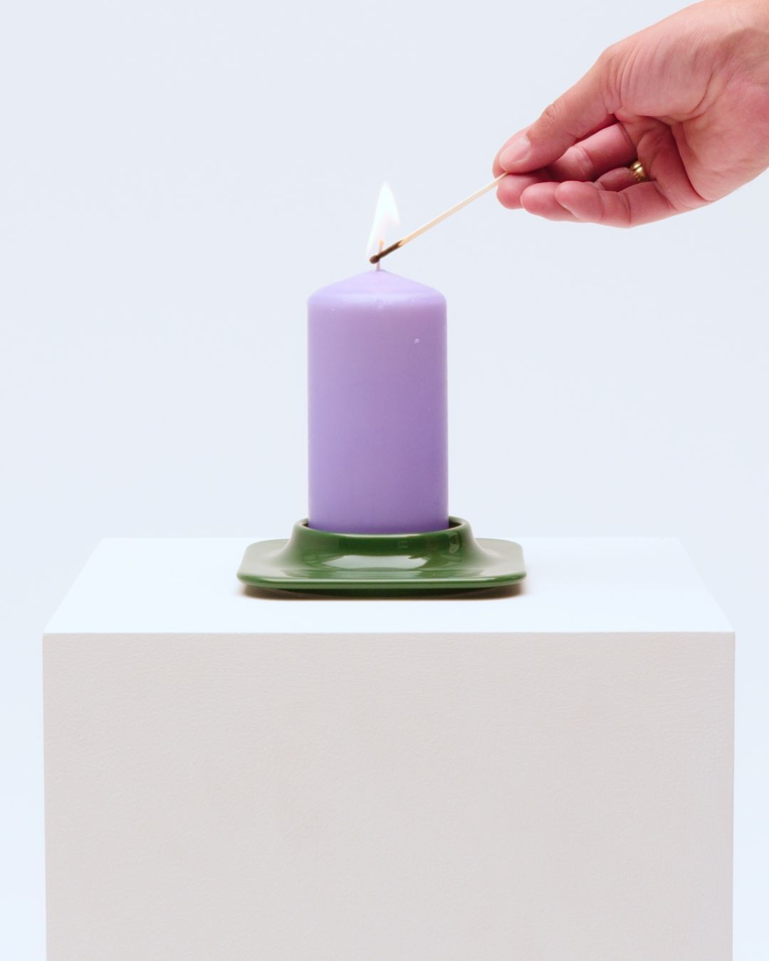 Hand lighting a large purple block scented candle in a green candleholder with a match.