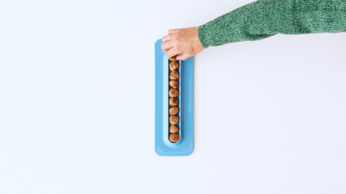 Hand reaching for a baby blue serving plate, touching a meatball in a row, seen from above.