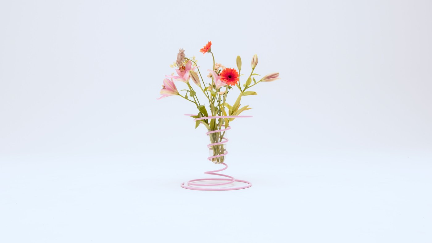 A pink spiral-shaped vase with a bouquet of green, pink and red flowers in it.