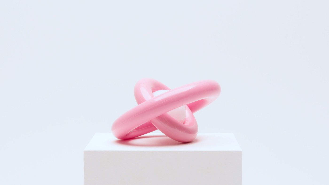 A pink sculptural lamp with its rings turned in opposite directions, standing on a pedestal.