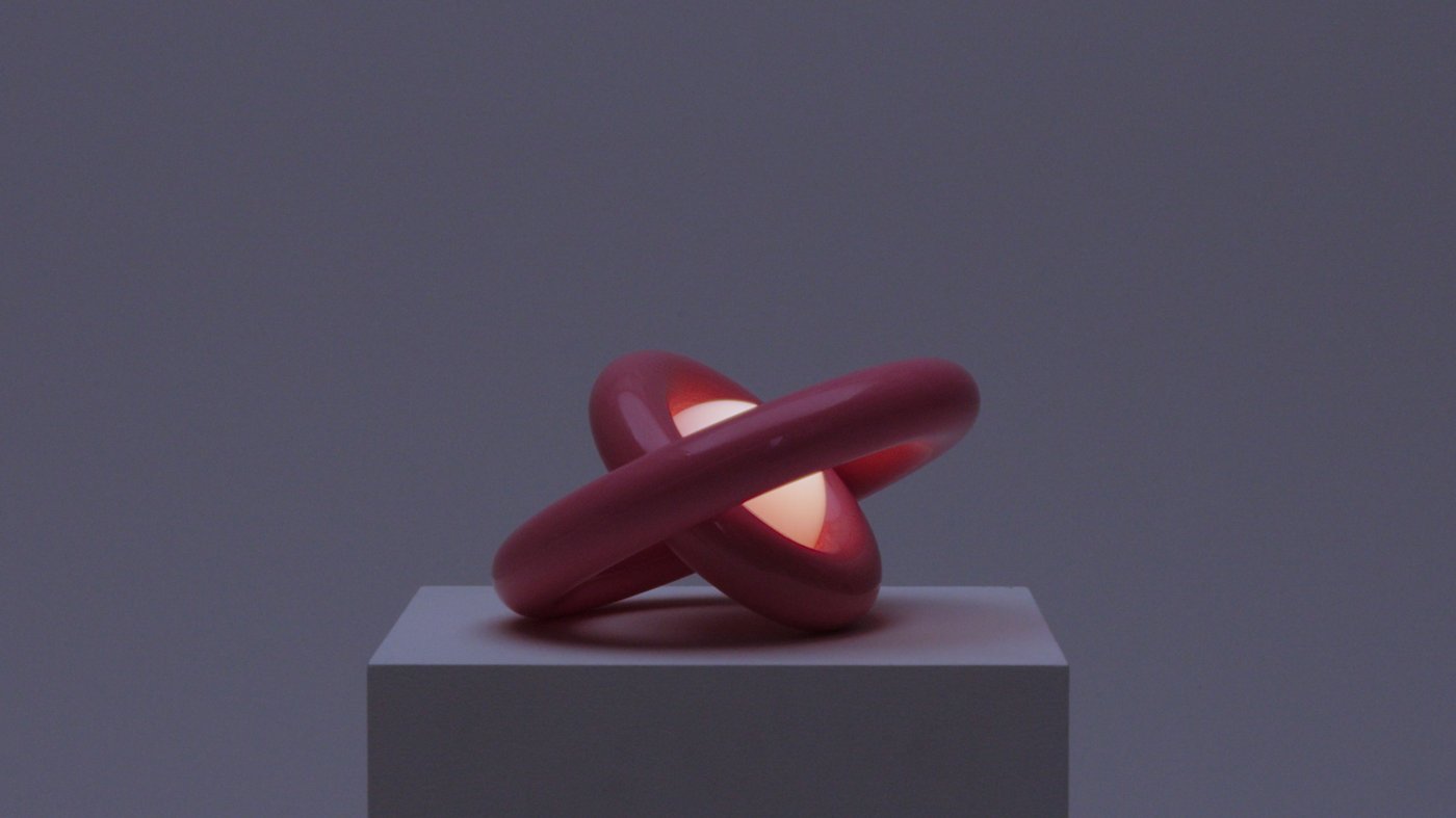 A pink sculptural lamp, lit in darkness, with its rings turned in opposite directions,