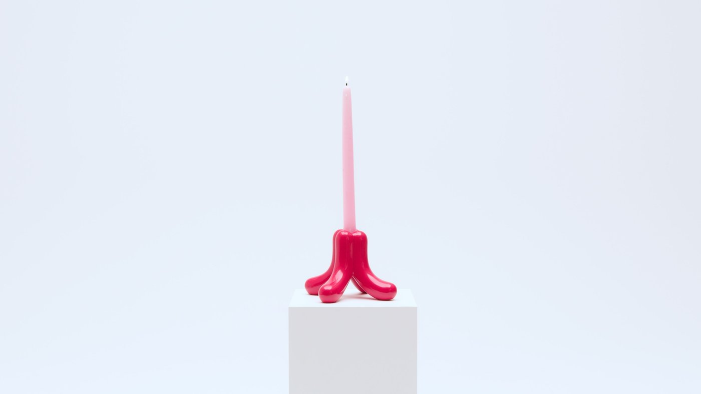 A red candlestick with a large pink pillar candle.