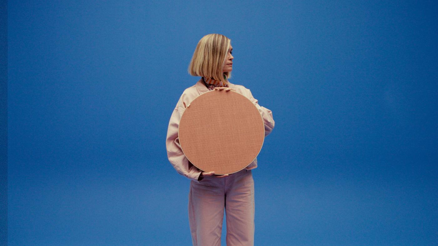 Designer Tekla Evelina Severin holds a large pink SOLSKYDD speaker against a blue background.