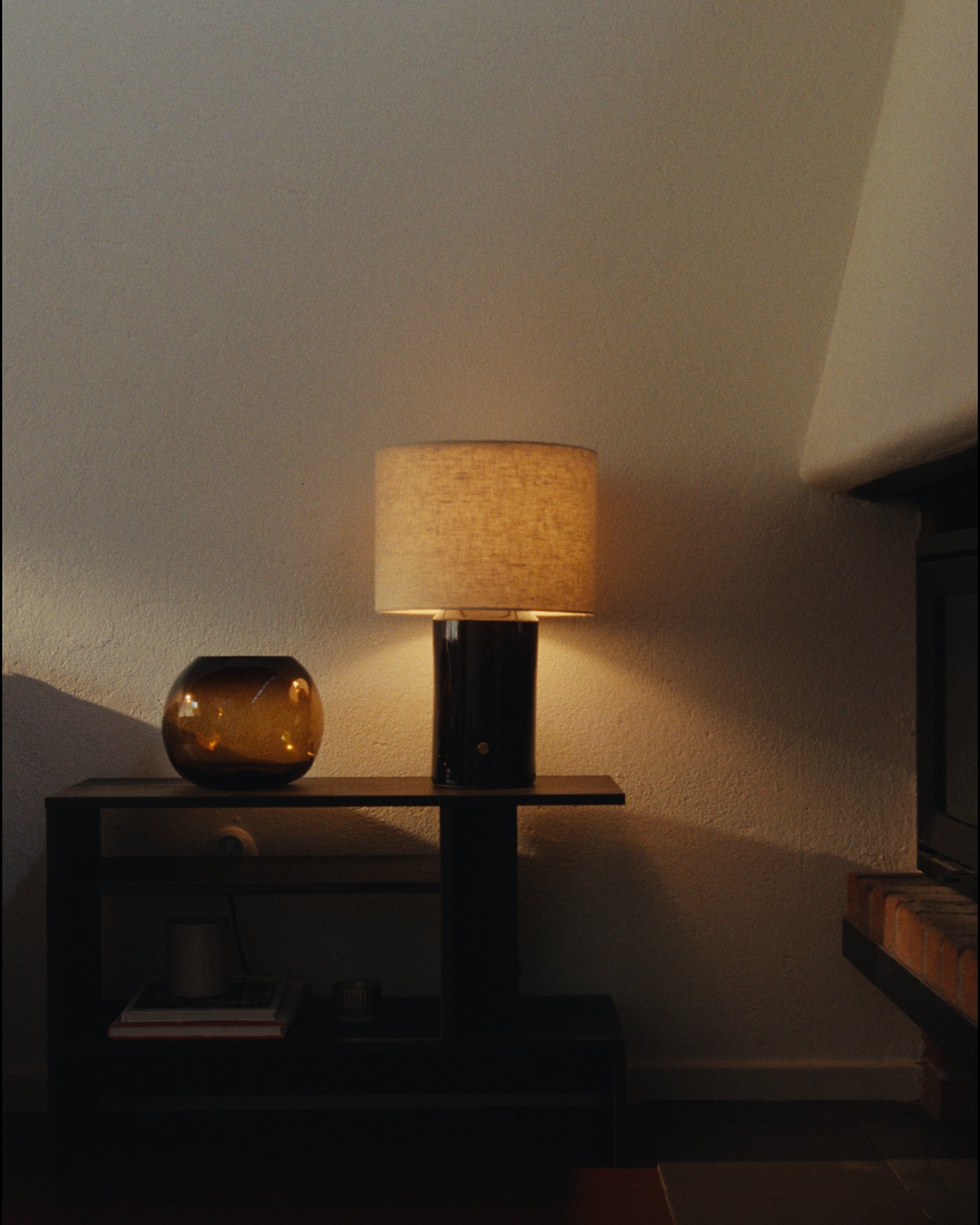 Table lamp with fabric shade on a side table next to a small amber glass vase.