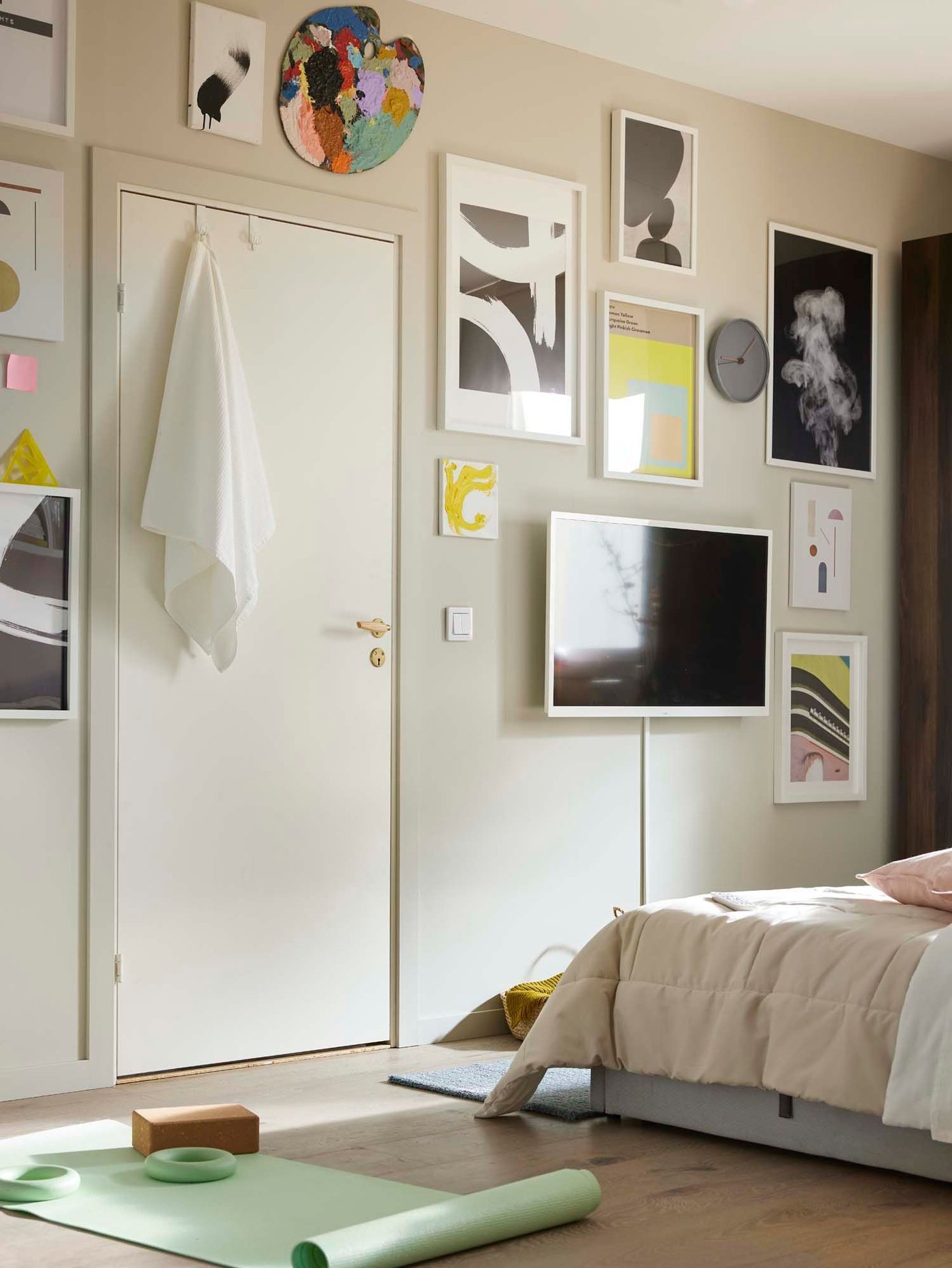 Slider image one: the wall at the end of a bed, with a door surrounded by wall art in a curated palette of black and white with accents of bright yellow and pink.