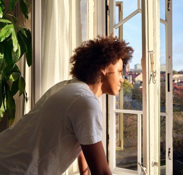 A person looking out of a window with afternoon sunshine coming into the room.
