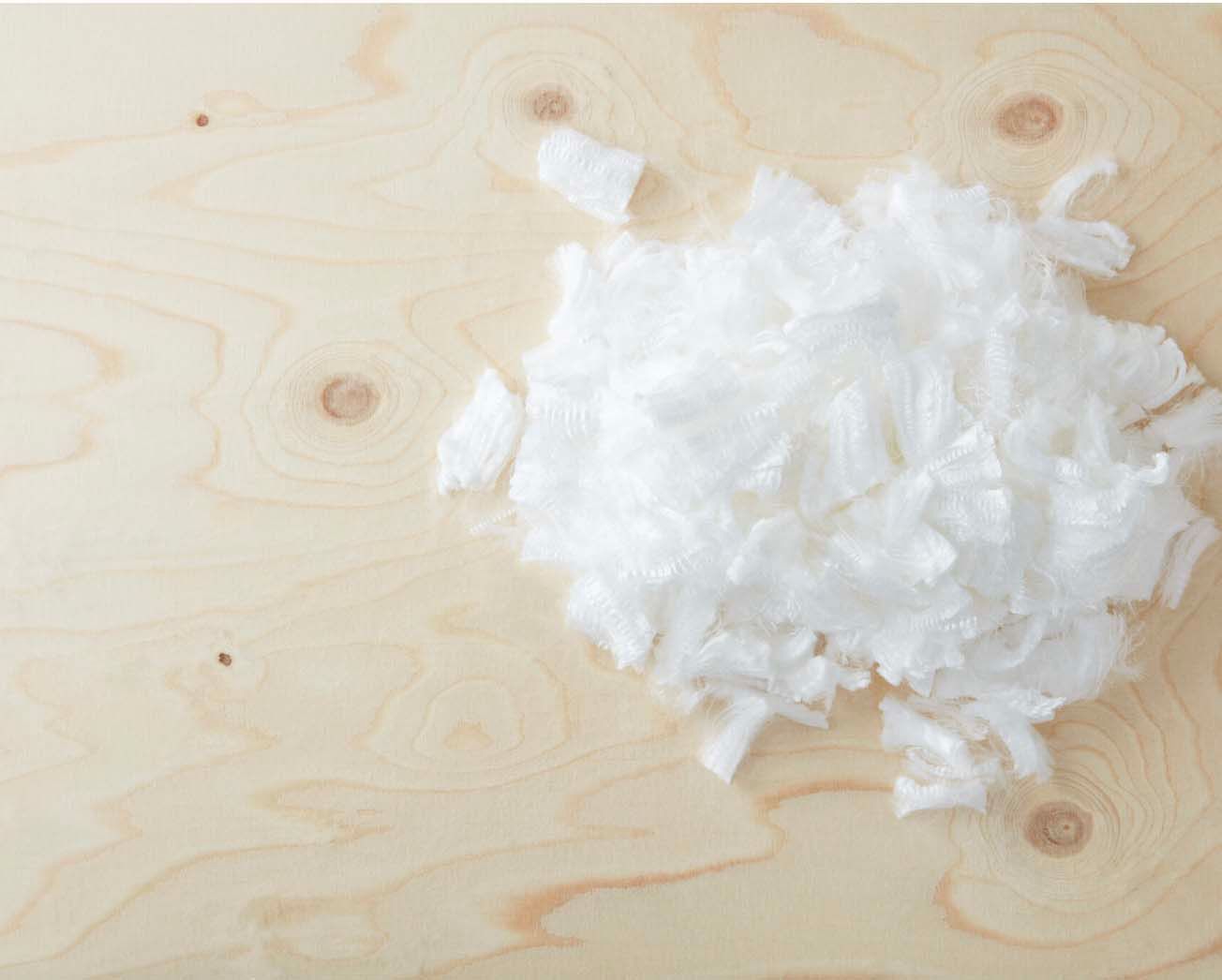A small heap of bio-based cellulose fibre on a light wooden surface.