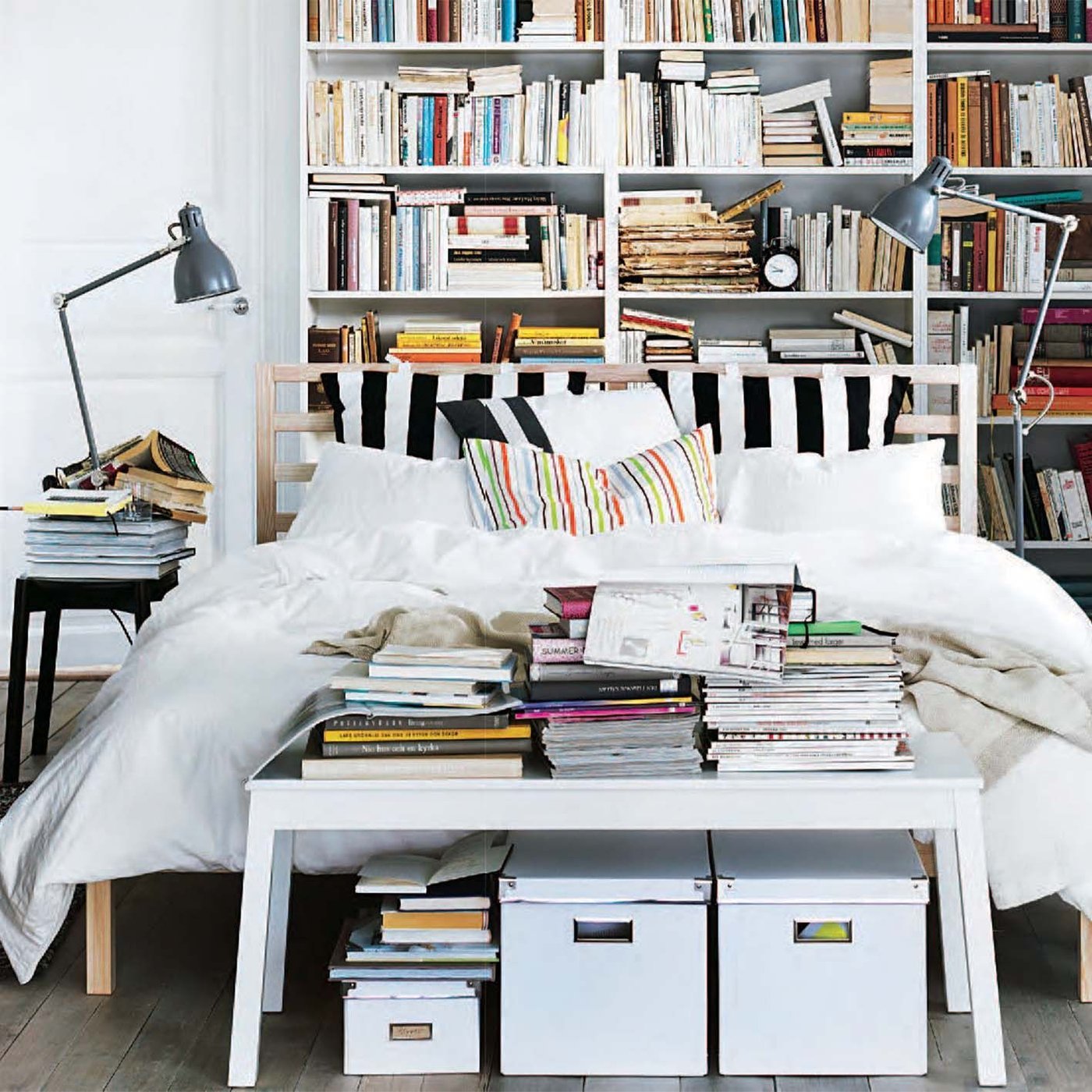 A white bedroom with coloured cushions on a white wood bed and light muslin fabric hanging from the ceiling.