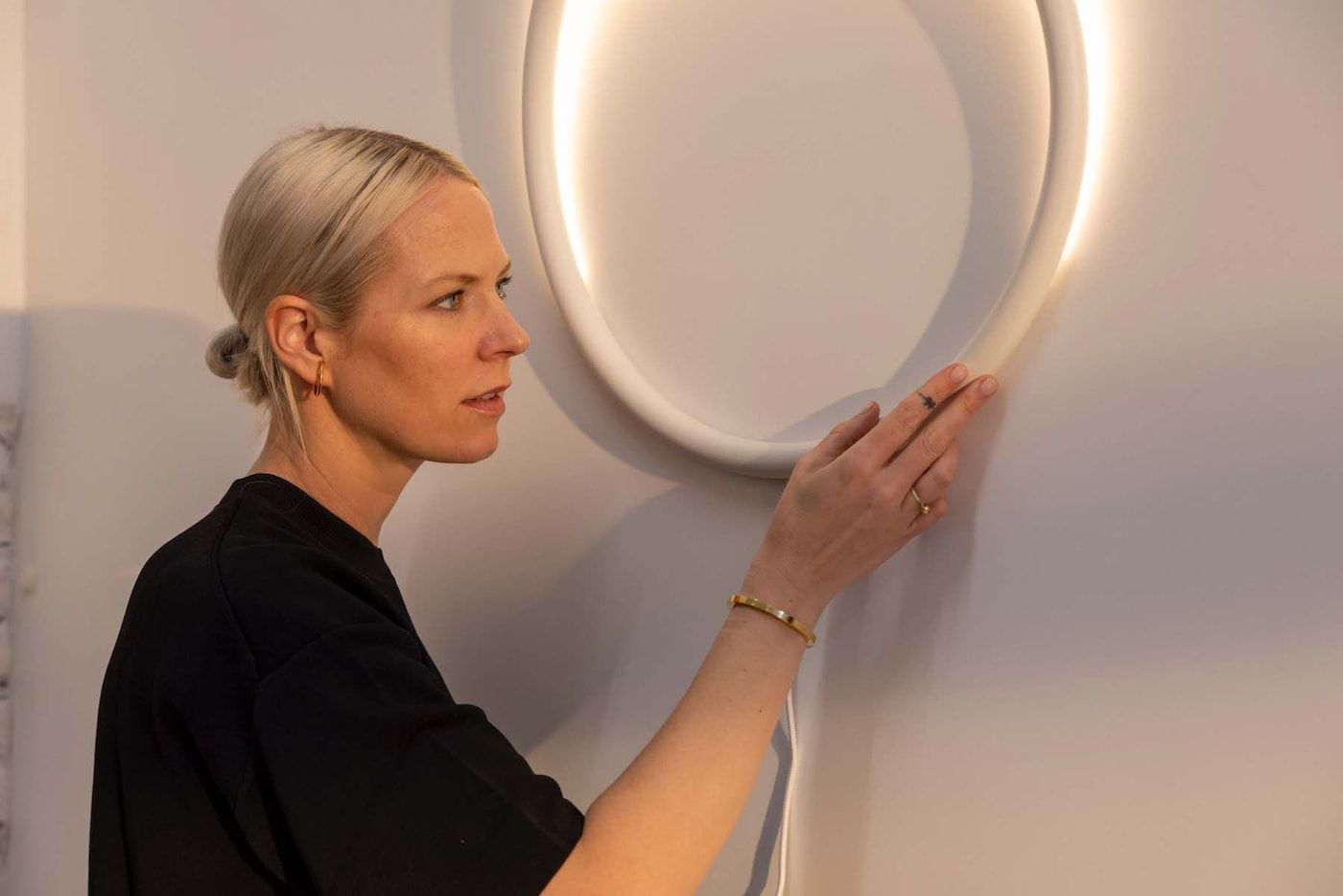 Sabine Marcelis touches a hoop-shaped wall-mounted lamp.