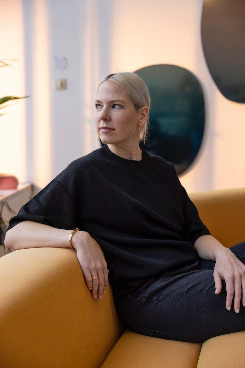 Designer Sabine Marcelis seated on an orange sofa.