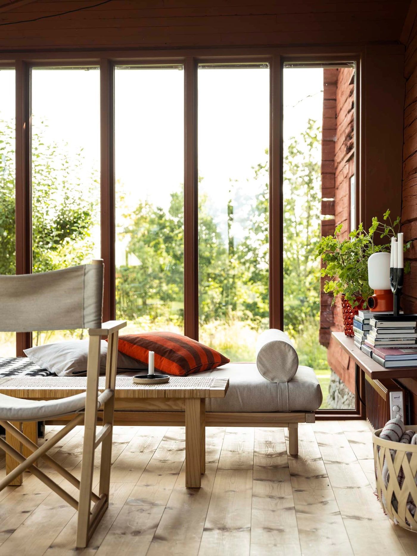A sitting area with a cushioned daybed. surrounded by glass windows overlooking a garden.