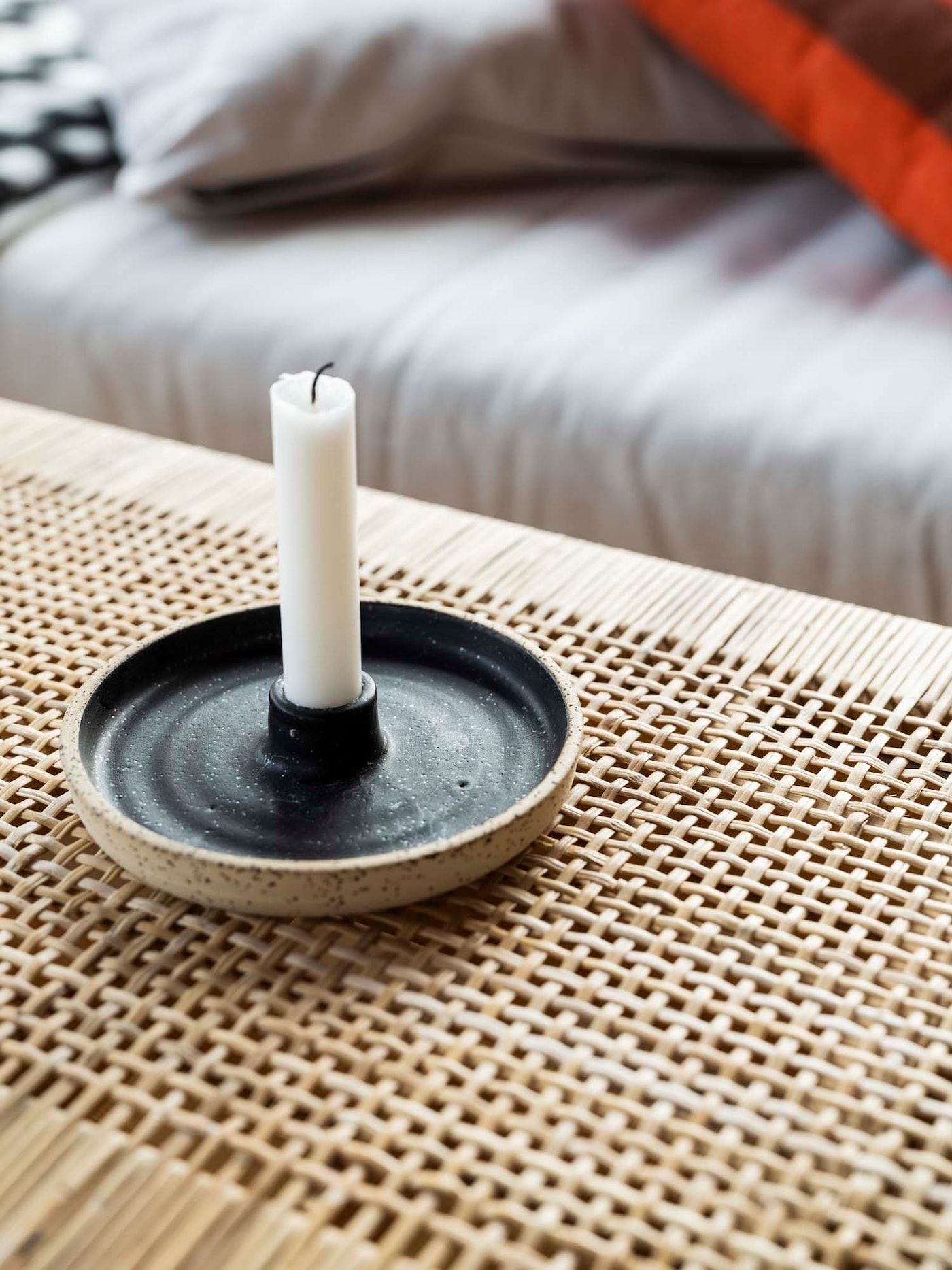 A ceramic candle holder and candle on a woven coffee table.